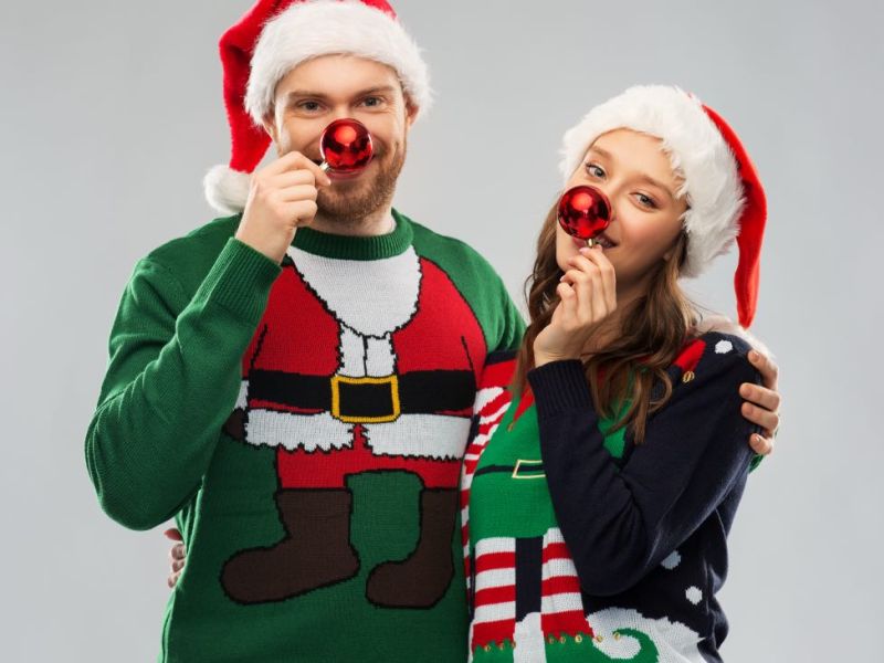 Ein glückliches junges Paar posiert vor der Kamera mit ausgefallenen Weihnachtspullis und Weihnachtsmützen.