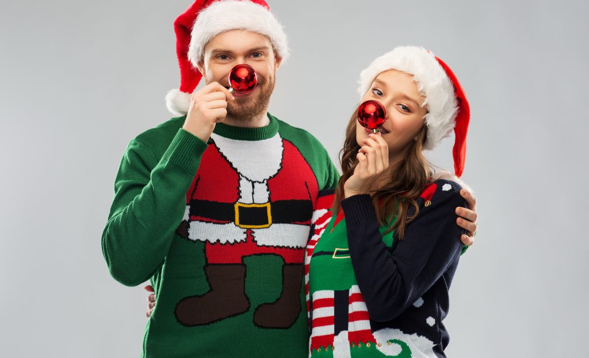 Ein glückliches junges Paar posiert vor der Kamera mit ausgefallenen Weihnachtspullis und Weihnachtsmützen.