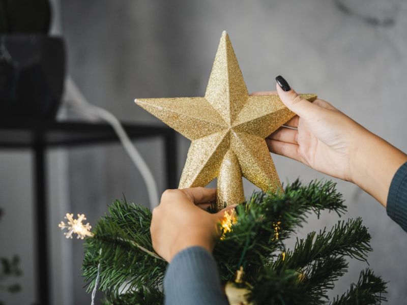 Eine Frau setzt einen Deko-Stern auf die Spitze eines Weihnachtsbaums.