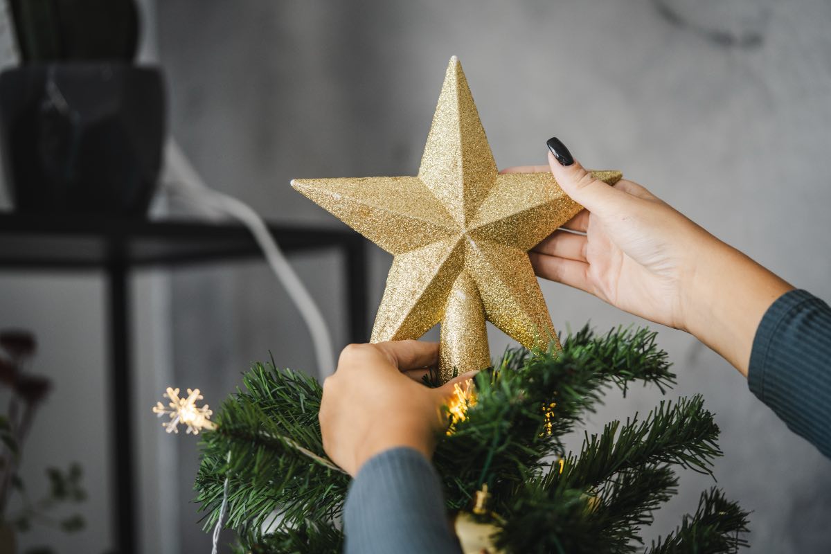 Eine Frau setzt einen Deko-Stern auf die Spitze eines Weihnachtsbaums.