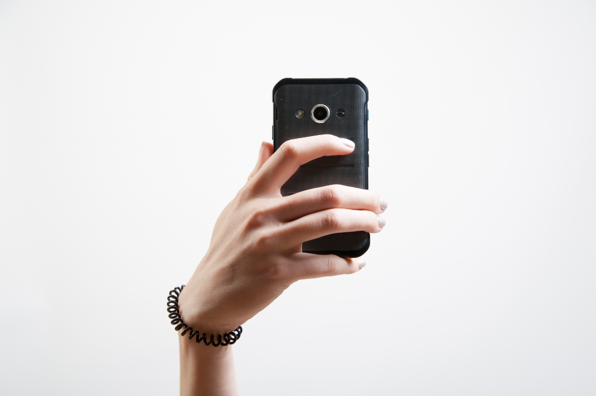 Die Hand eines jungen Mädchens hält ein Smartphone hoch, um ein Selfie zu machen.