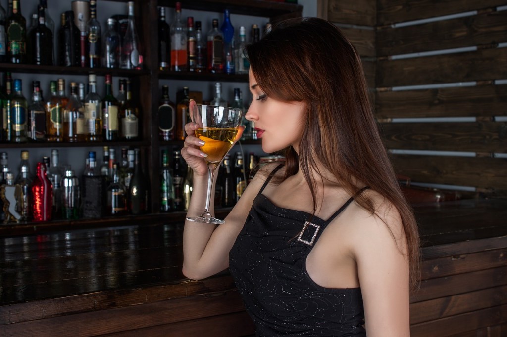 Eine junge, attraktive Frau trinkt einen Cocktail in einer Bar.