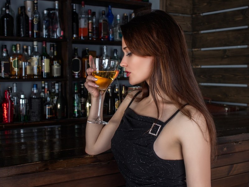 Eine junge, attraktive Frau trinkt einen Cocktail in einer Bar.