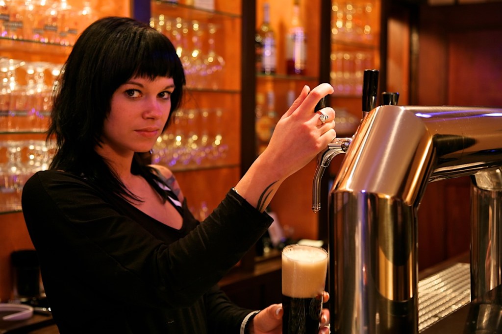 Eine junge Kellnerin zapft ein Bier in einer Kneipe.