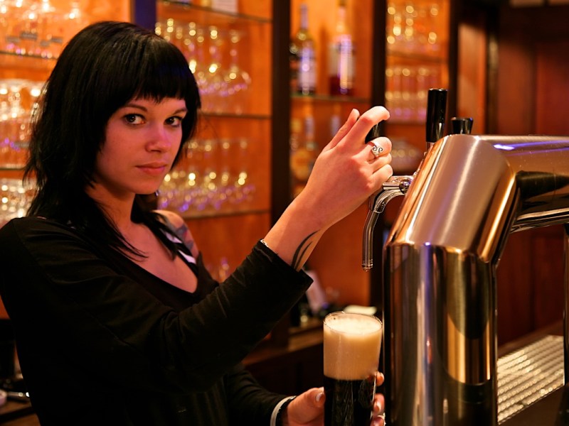 Eine junge Kellnerin zapft ein Bier in einer Kneipe.