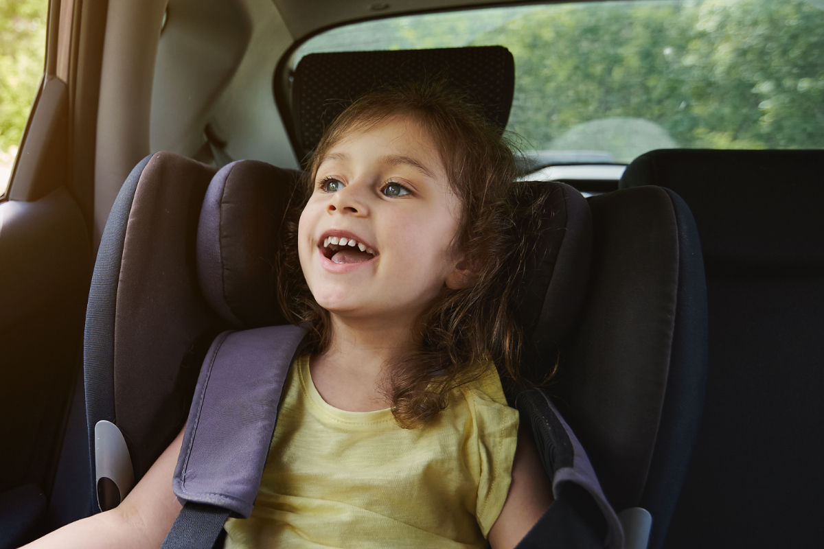 Ein kleines Mädchen sitzt angeschnallt im Auto und lacht.