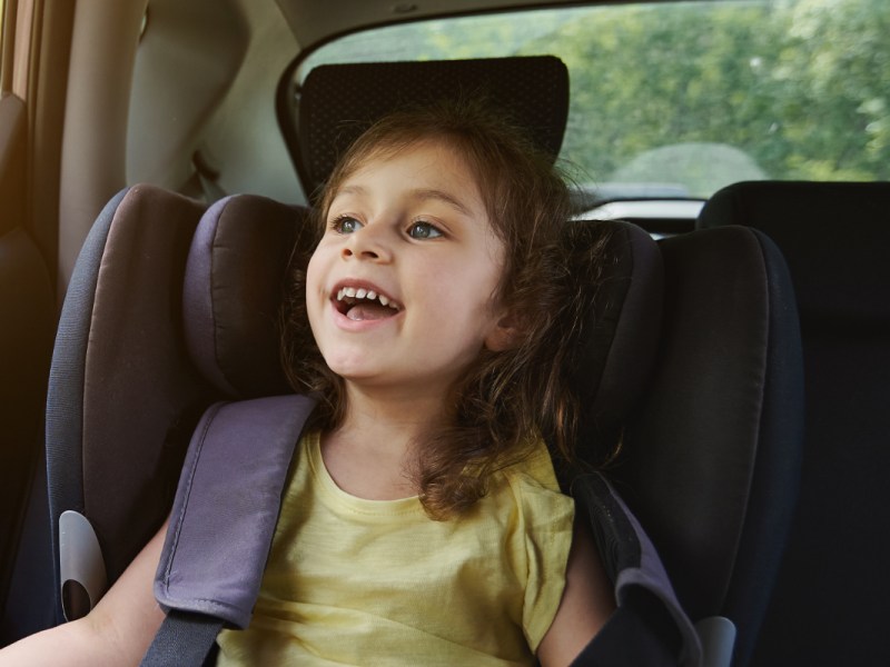 Ein kleines Mädchen sitzt angeschnallt im Auto und lacht.