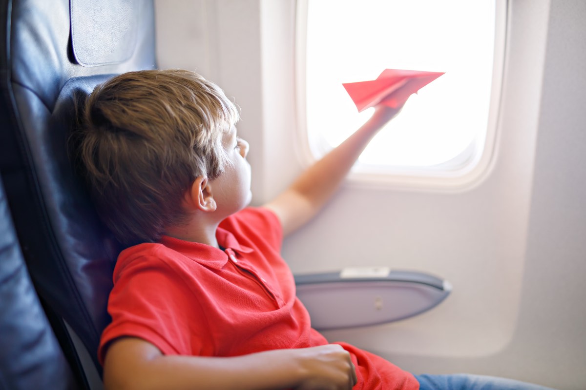 Ein kleiner Junge spielt mit einem roten Papierflugzeug während eines Flugs.
