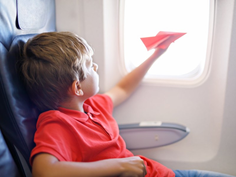 Ein kleiner Junge spielt mit einem roten Papierflugzeug während eines Flugs.