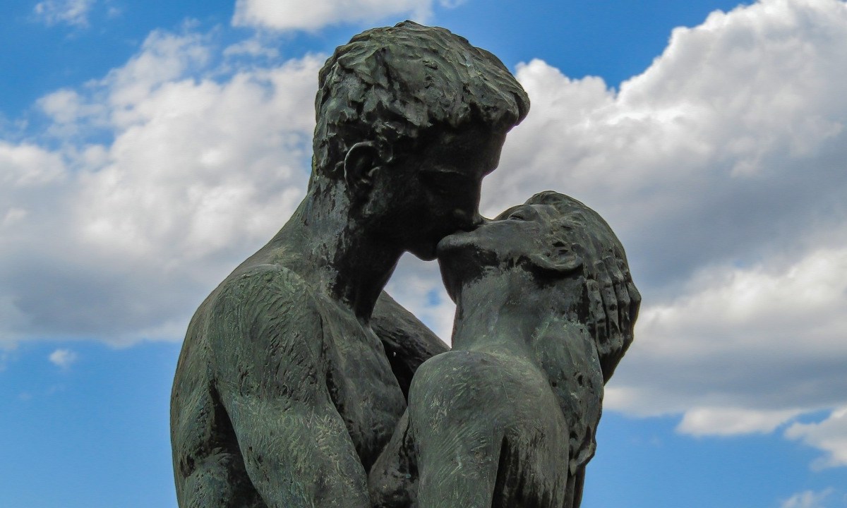 Eine Statue, die ein küssendes Paar zeigt, vor blauem Himmel.