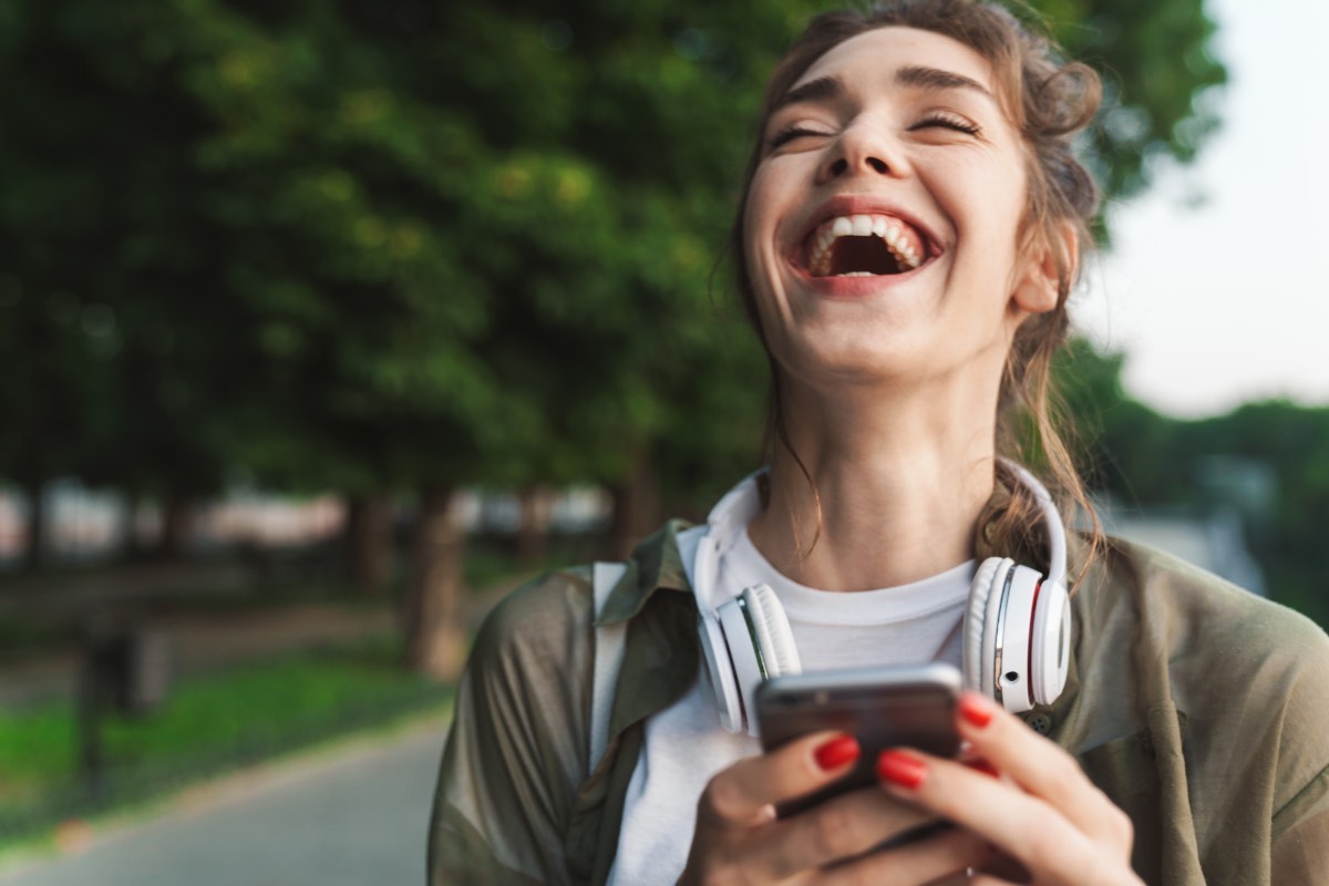 Ein Bild einer jungen, lachenden Frau, die auf ihr Smartphone schaut.