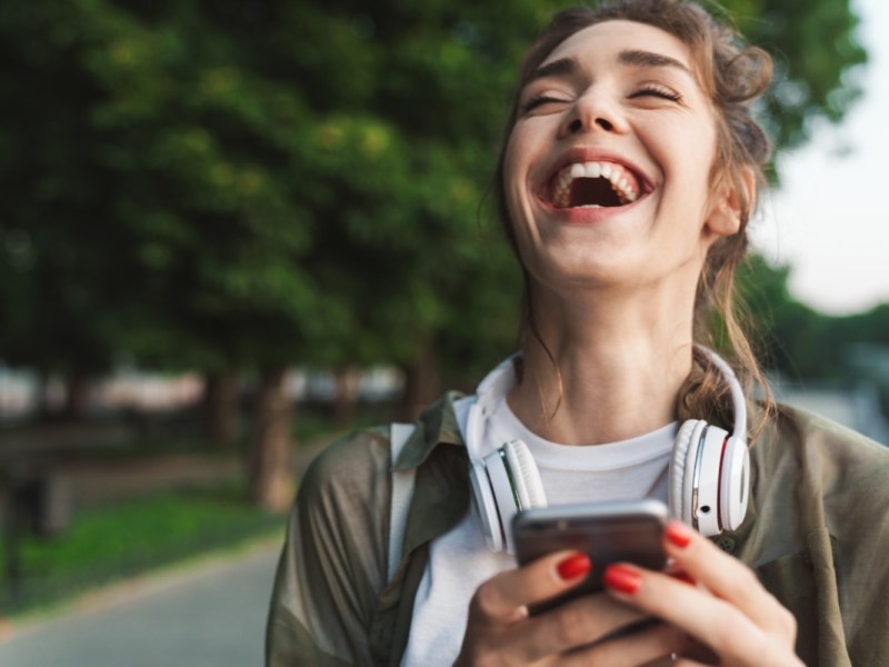 Ein Bild einer jungen, lachenden Frau, die auf ihr Smartphone schaut.