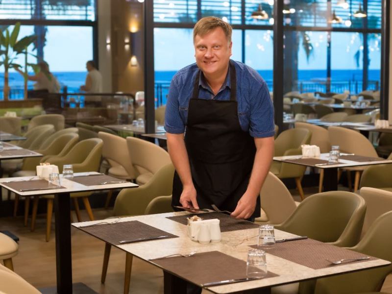 Ein lächelnder Kellner deckt einen Tisch in einem Restaurant.