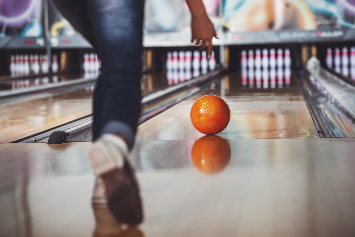 Eine Frau beim Bowling wirft eine Bowlingkugel.