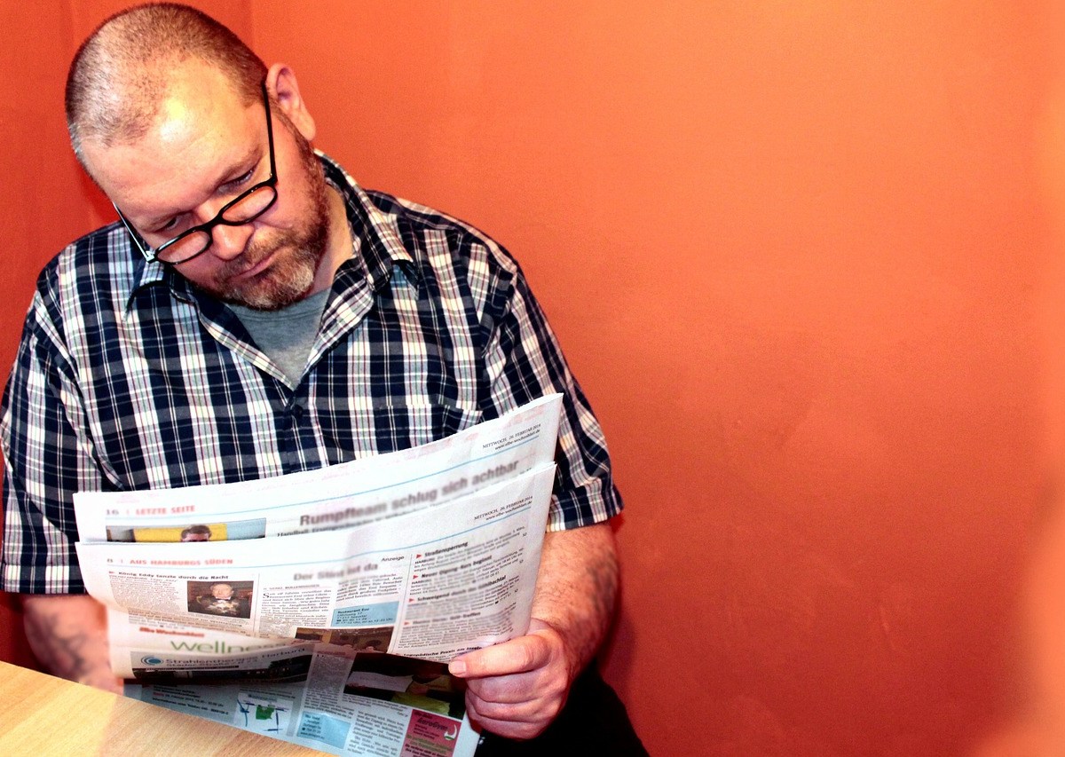 Ein Mann mit Brille und kariertem Hemd liest eine Zeitung.