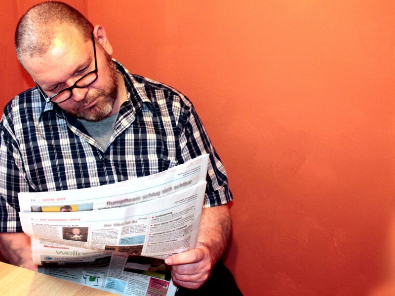Ein Mann mit Brille und kariertem Hemd liest eine Zeitung.
