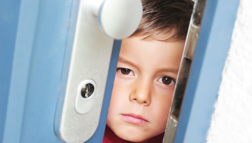 Ein blonder kleiner Junge schaut durch einen Türspalt.