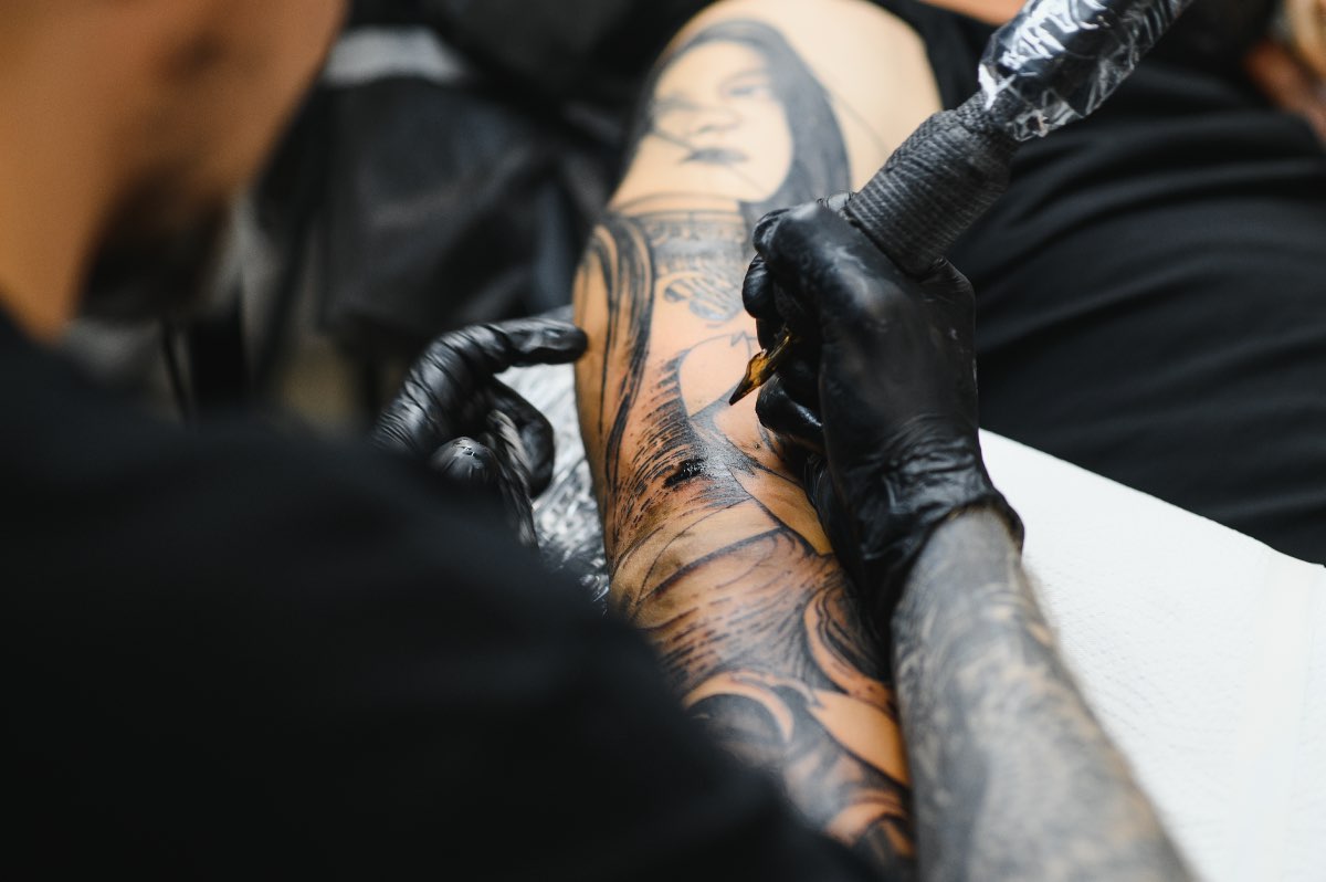 Ein Tätowierer sticht einem Kunden ein Tattoo auf den Arm.