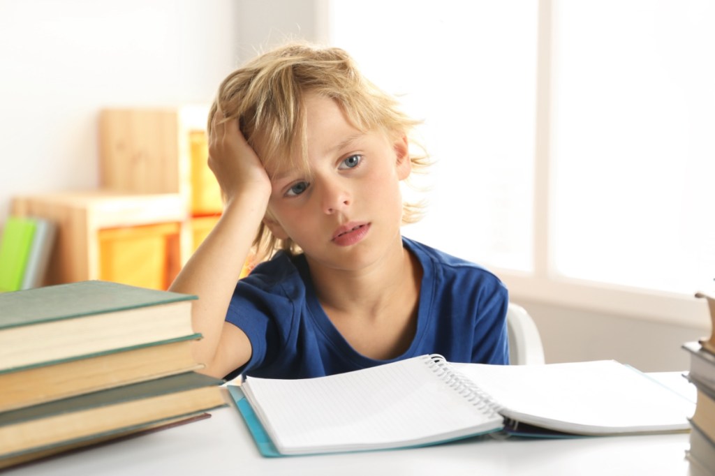 Ein nachdenklicher kleiner, blonder Junge sitzt an seinen Hausaufgaben für die Schule.
