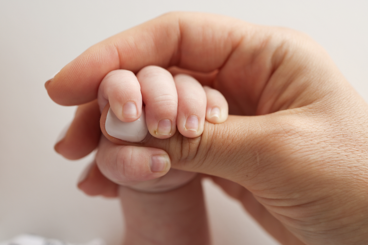 Ein Baby umfasst mit der Hand den Daumen seines Vaters.