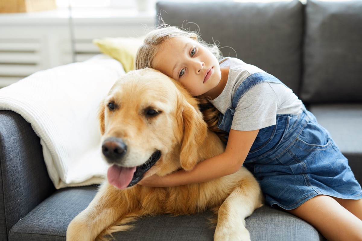 Ein kleines blondes Mädchen umarmt einen Labrador.