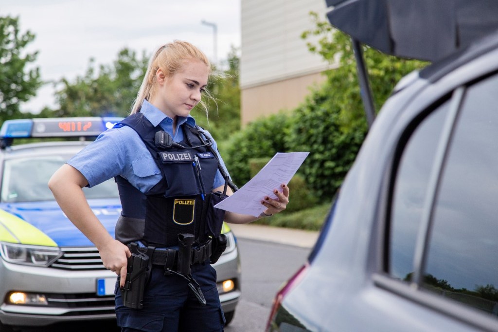 Eine Polizistin prüft die Fahrzeugpapiere eines Autofahrers