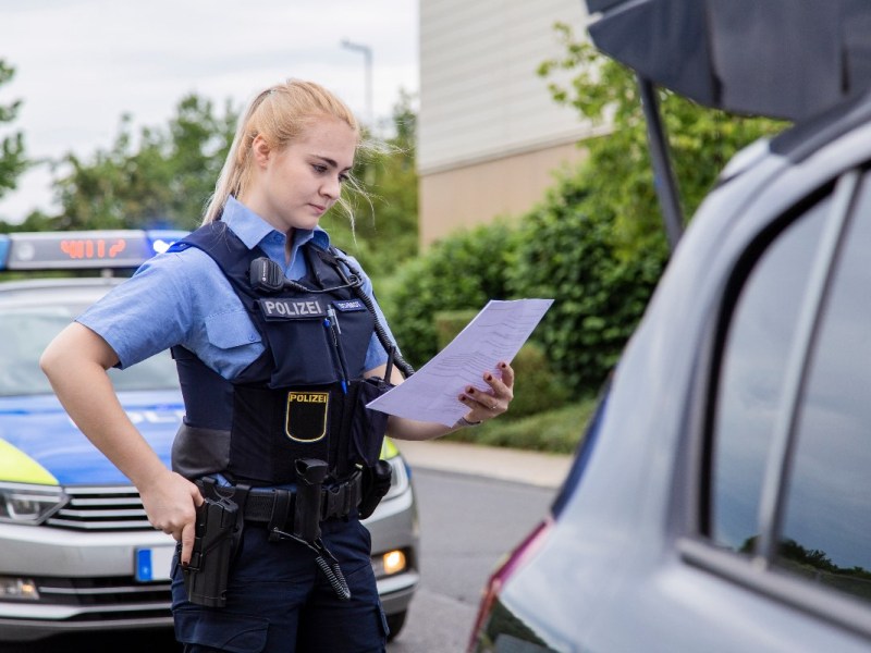 Eine Polizistin prüft die Fahrzeugpapiere eines Autofahrers