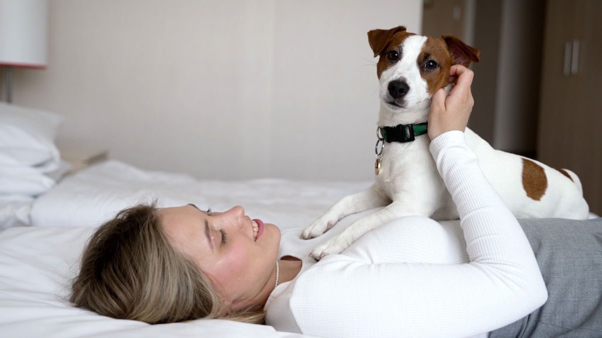 Eine Frau kuschelt mit einem Hund auf einem Hotel-Bett.