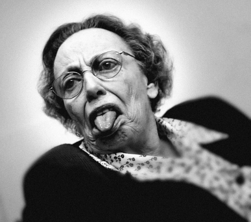 Ein Schwarzweiß-Foto von einer Rentnerin, die frech ihre Zunge herausstreckt.