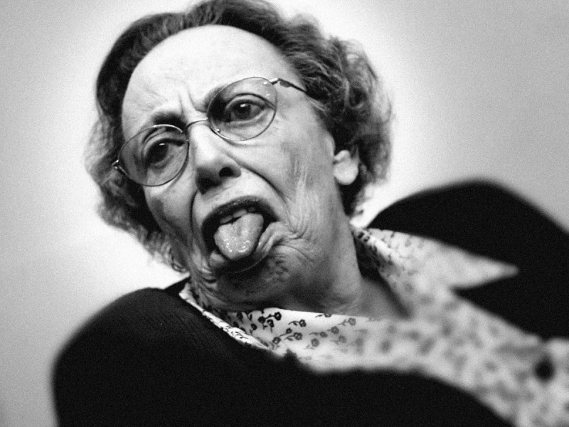 Ein Schwarzweiß-Foto von einer Rentnerin, die frech ihre Zunge herausstreckt.
