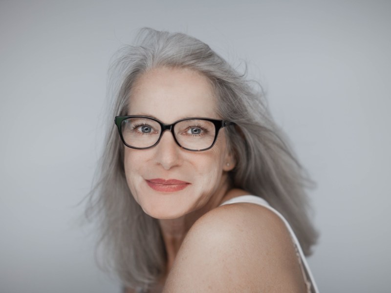 Eine junge selbstbewusste Frau mit Brille und grauen Haaren.