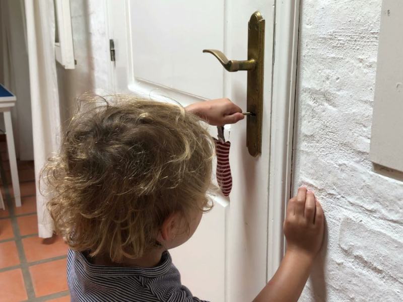Ein kleiner, blonder Junge schließt mit einem Schlüssel eine Tür auf.