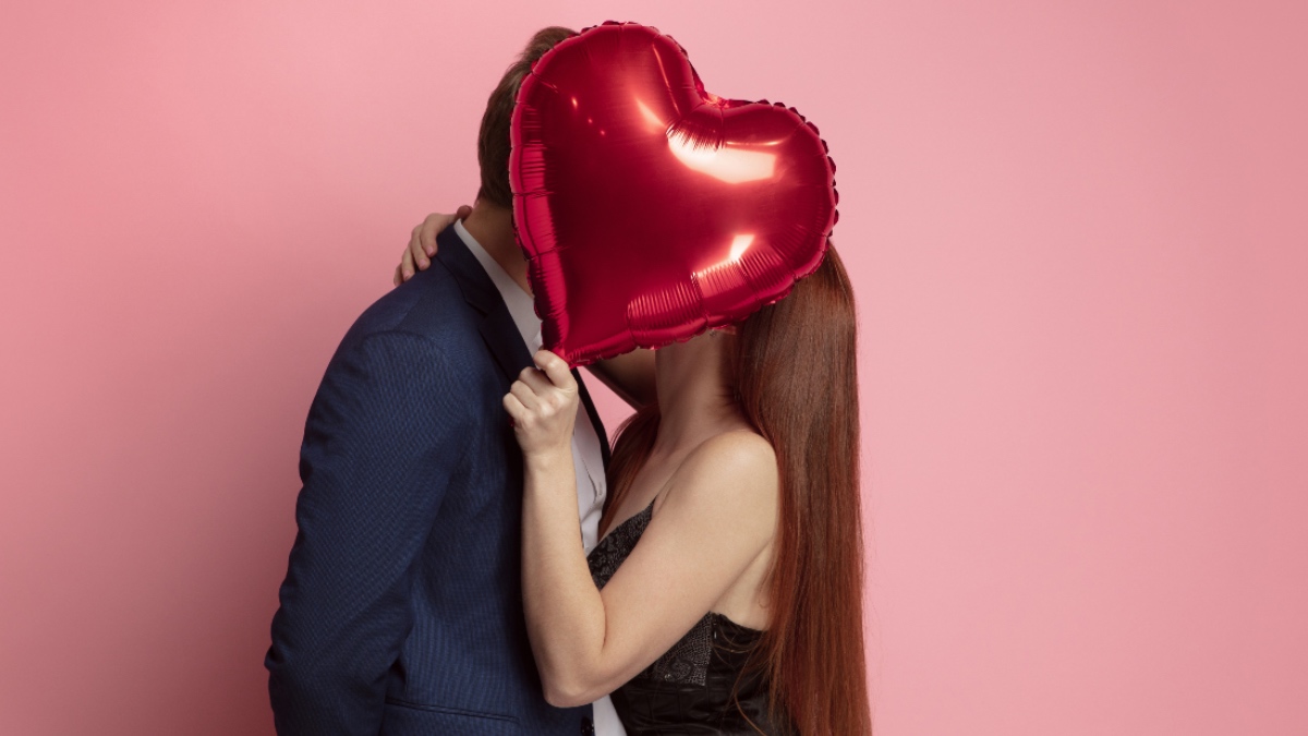 Ein Paar, das sich hinter einem Ballon in Herzform küsst.
