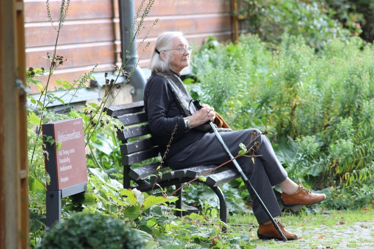 Eine alte Frau sitzt auf einer Parkbank.