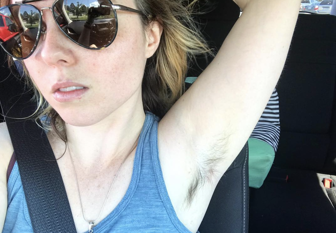 Frau mit Sonnenbrille zeigt haarige Achsel