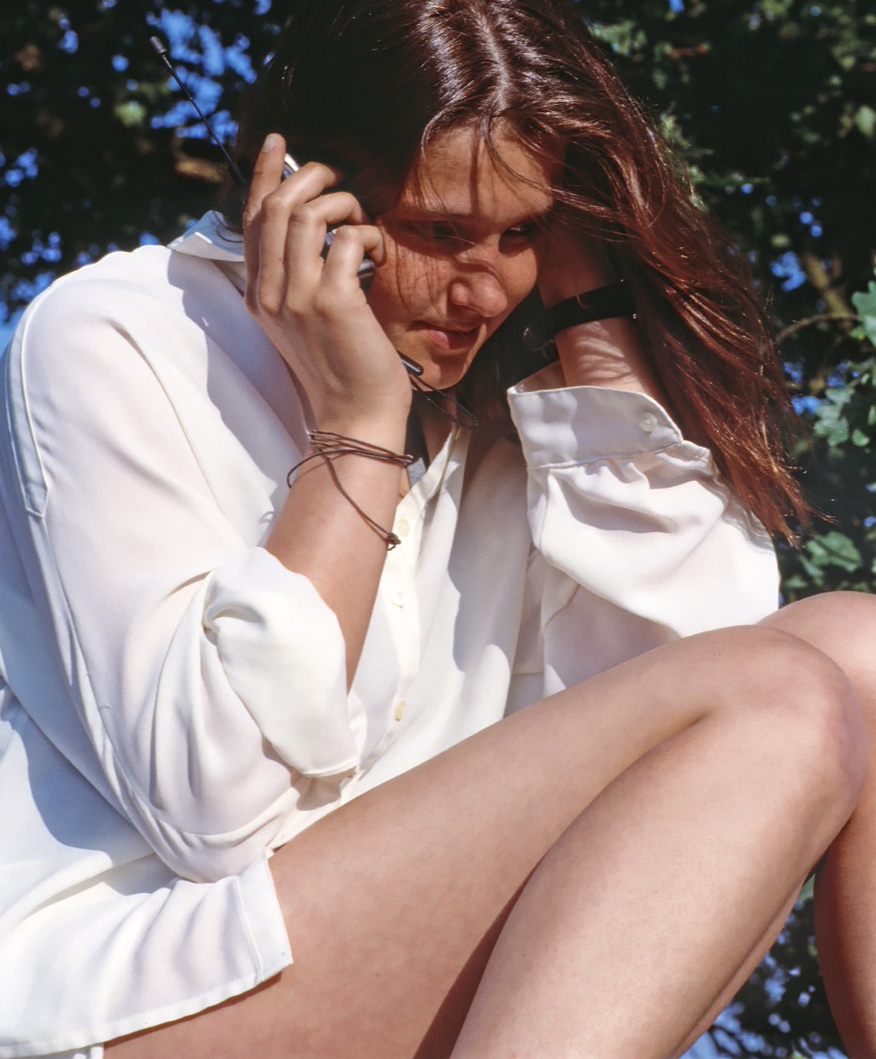 Eine Frau mit weisser Bluse sitzt auf einer Parkbank und telefoniert