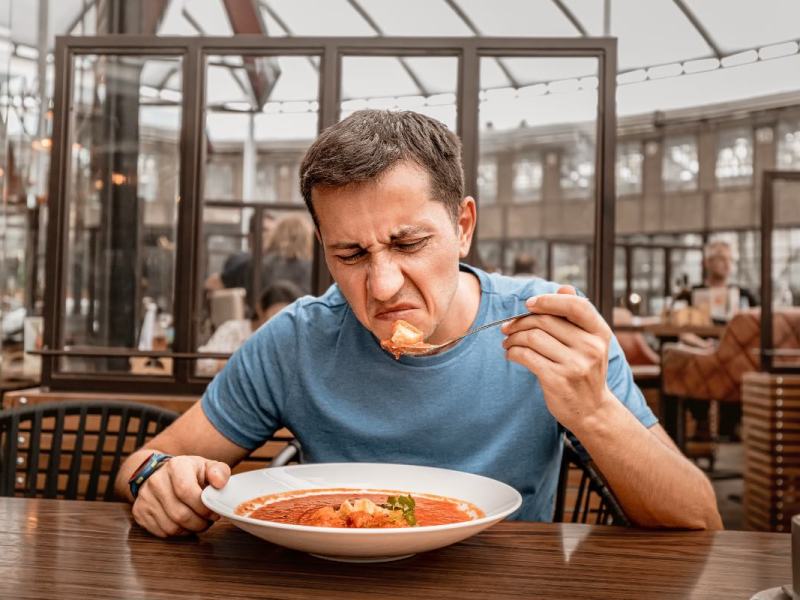 Ein unzufriedener Gast in einem Restaurant verzieht angewidert das Gesicht beim Essen.