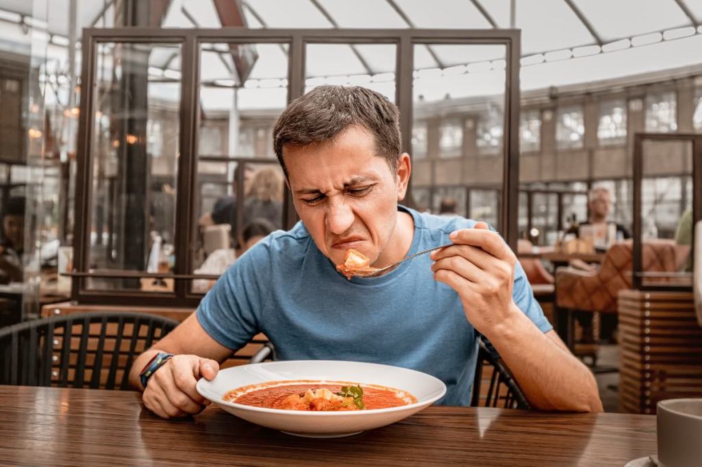 Ein unzufriedener Gast in einem Restaurant verzieht angewidert das Gesicht beim Essen.