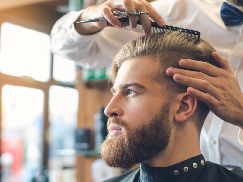 Ein junger Mann bekommt bei einem Friseur die Haare geschnitten.