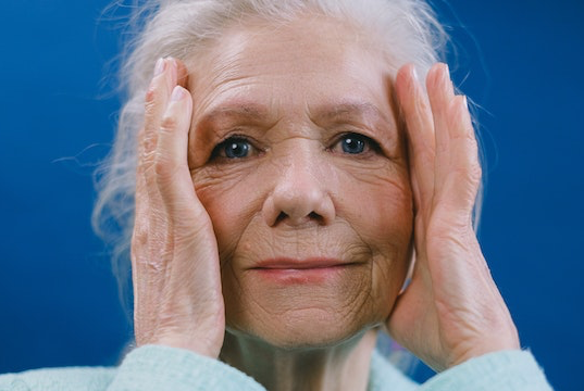 Eine alte Frau mit grauen Haaren hat Kopfschmerzen und hält sich den Kopf