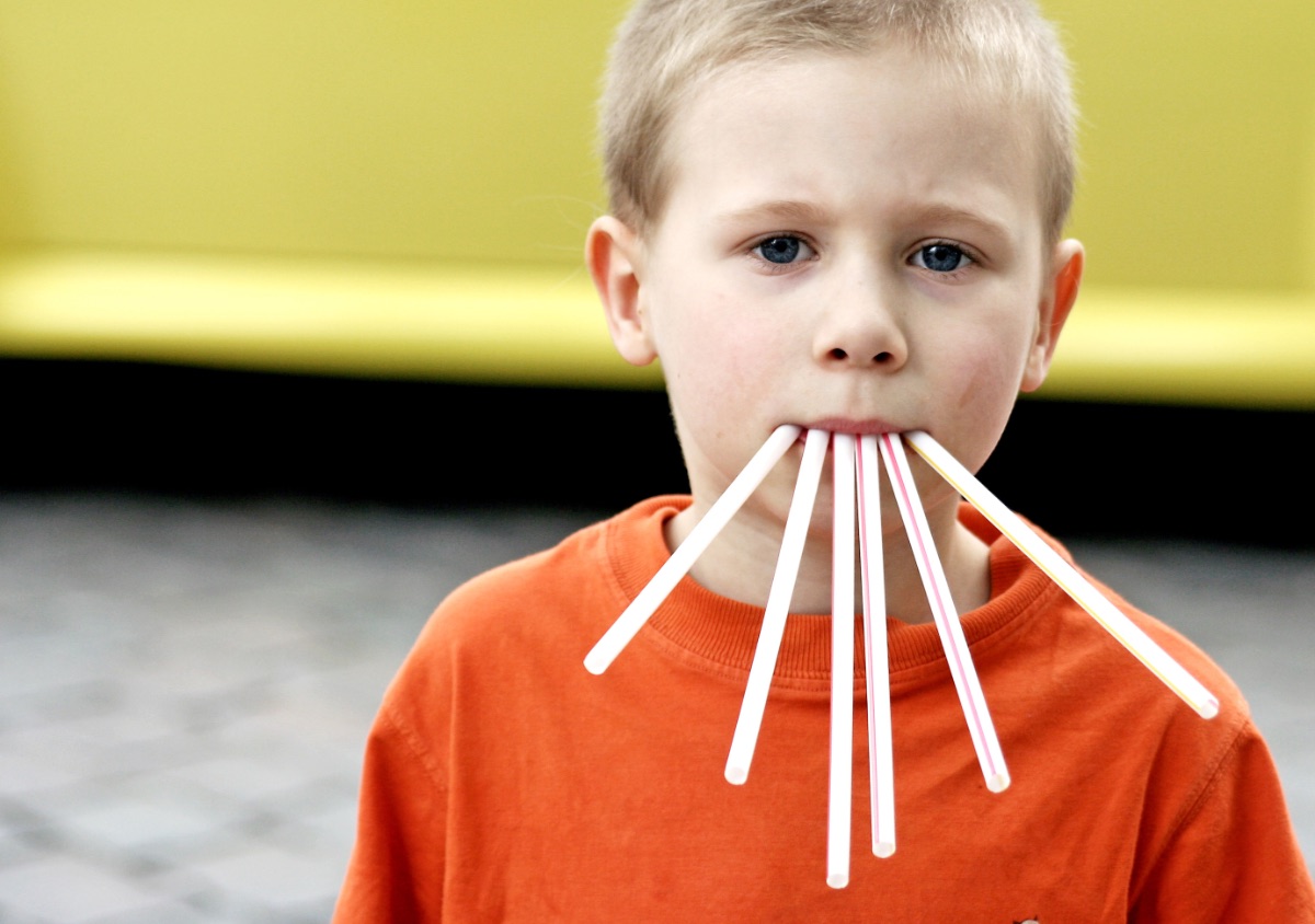 Ein lustiges Bild von einem kleinen Jungen, der sechs Strohhalme im Mund hat.