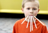 Ein lustiges Bild von einem kleinen Jungen, der sechs Strohhalme im Mund hat.