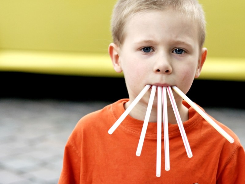 Ein lustiges Bild von einem kleinen Jungen, der sechs Strohhalme im Mund hat.