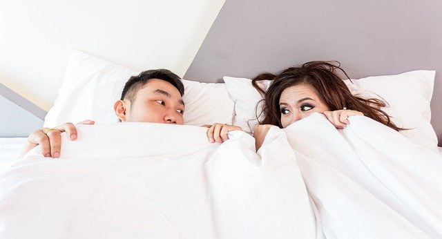 Ein Mann und eine Frau liegen zusammen im Bett und ziehen die Decke hoch