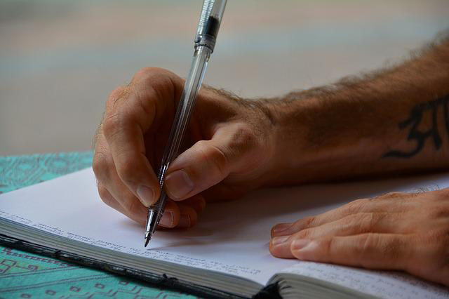 Eine männliche Hand mit Kugelschreiber schreibt in ein Heft