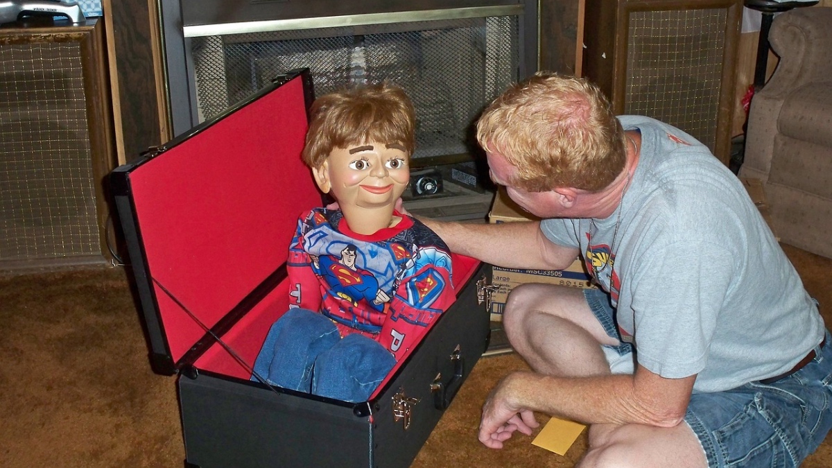Ein Bauchredner holt eine Marionette mit Superman-Kostüm aus einer Kiste
