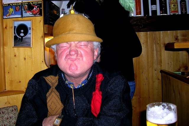 Ein Mann mit Hut trinkt ein Bier in einer Kneipe und schneidet eine Grimasse