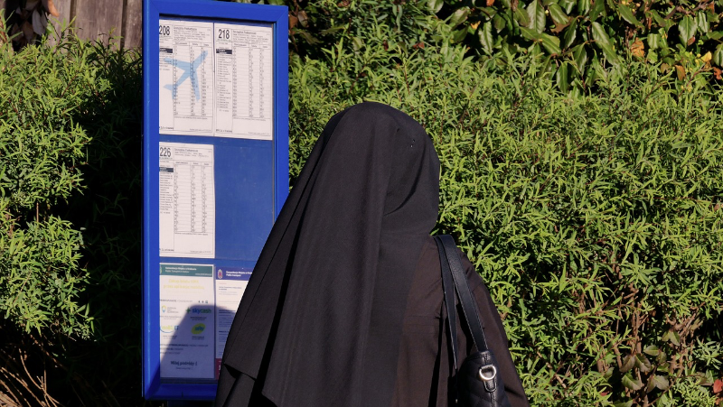 Eine Nonne wartet an einer Bushaltestelle