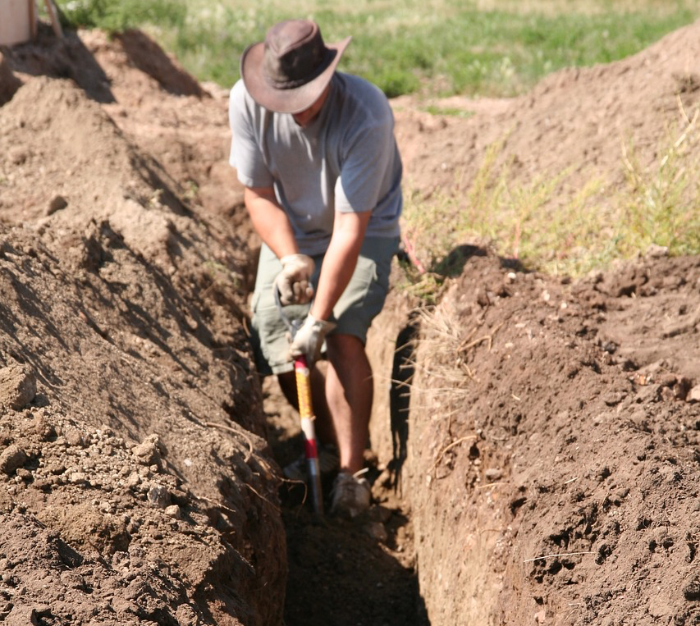 Ein Mann mit kurzer Hose und Hut gräbt mit einer Schaufel ein Loch