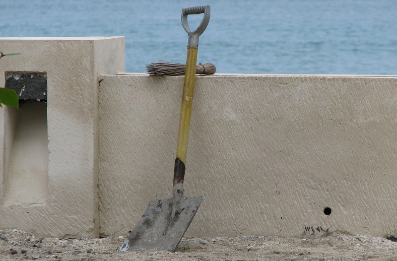 Eine Schaufel lehnt an einer Mauer und im Hintergrund ist das Meer zu sehen